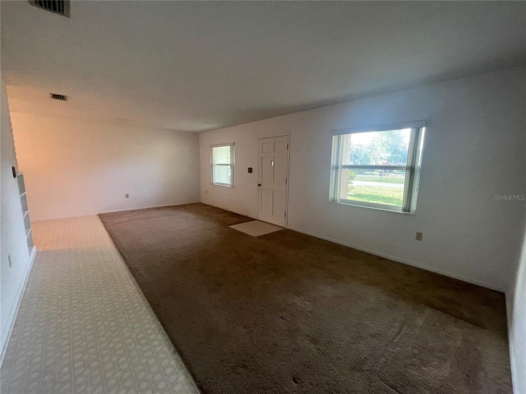 A living room features brown carpeting, white walls, a front door, and two windows — 23 LONESOME PINE TRAIL, YALAHA, FL