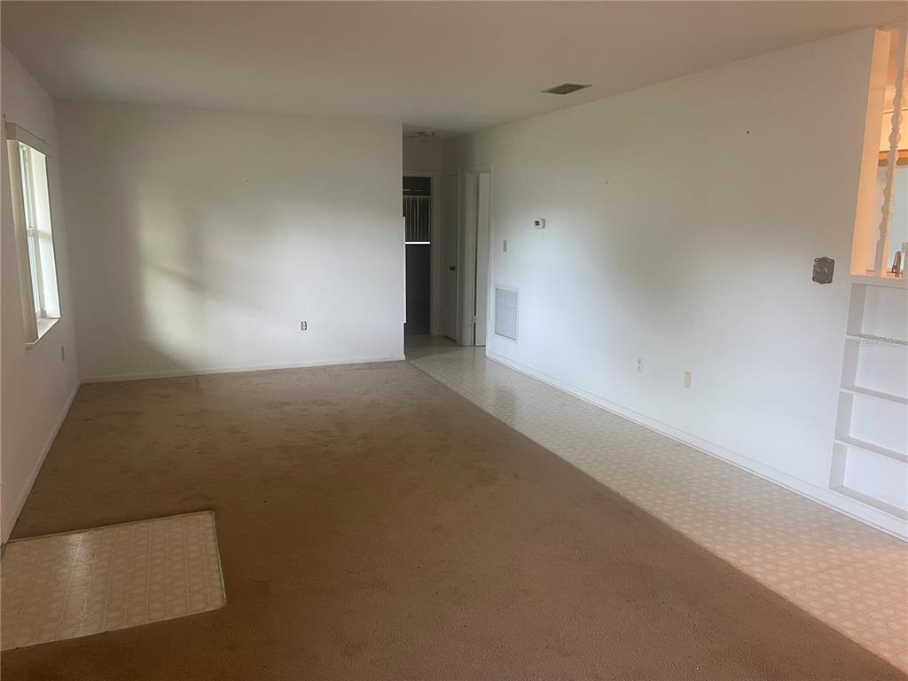 A living room with brown carpeting, white walls, and a tiled entryway area — 23 LONESOME PINE TRAIL, YALAHA, FL