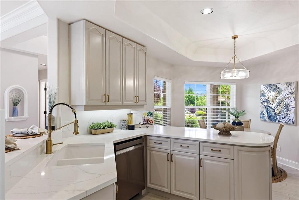 A kitchen features white cabinetry, quartz countertops, a gold faucet, and an adjacent dining area — 1703 STARLING DRIVE UNIT 1703, SARASOTA, FL