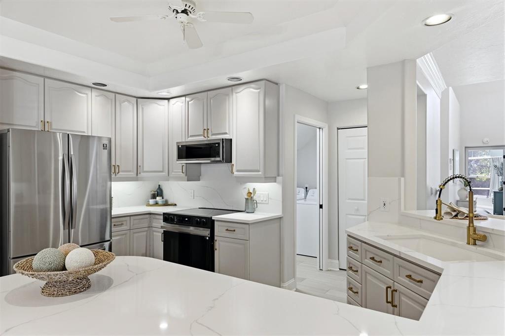 A modern kitchen features light gray cabinets, white quartz countertops, and stainless steel appliances — 1703 STARLING DRIVE UNIT 1703, SARASOTA, FL