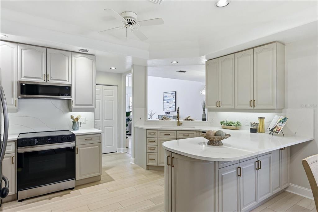 A kitchen features light gray cabinets, white quartz countertops, stainless steel appliances, and wood-look flooring — 1703 STARLING DRIVE UNIT 1703, SARASOTA, FL