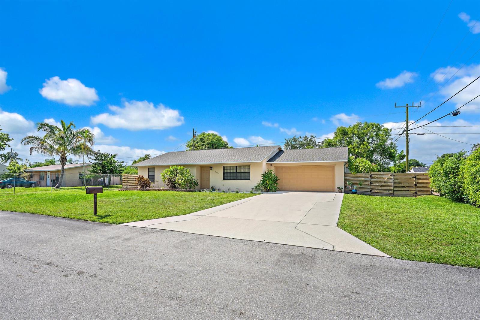 A single-story house with a beige exterior, a two-car garage, and a concrete driveway — 9090 Palladium Place, Lake Worth FL 33467, LAKE WORTH, FL