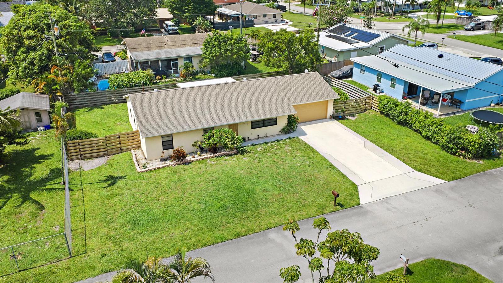 An aerial view shows a single-story house with a tan exterior, shingled roof, and driveway — 9090 Palladium Place, Lake Worth FL 33467, LAKE WORTH, FL
