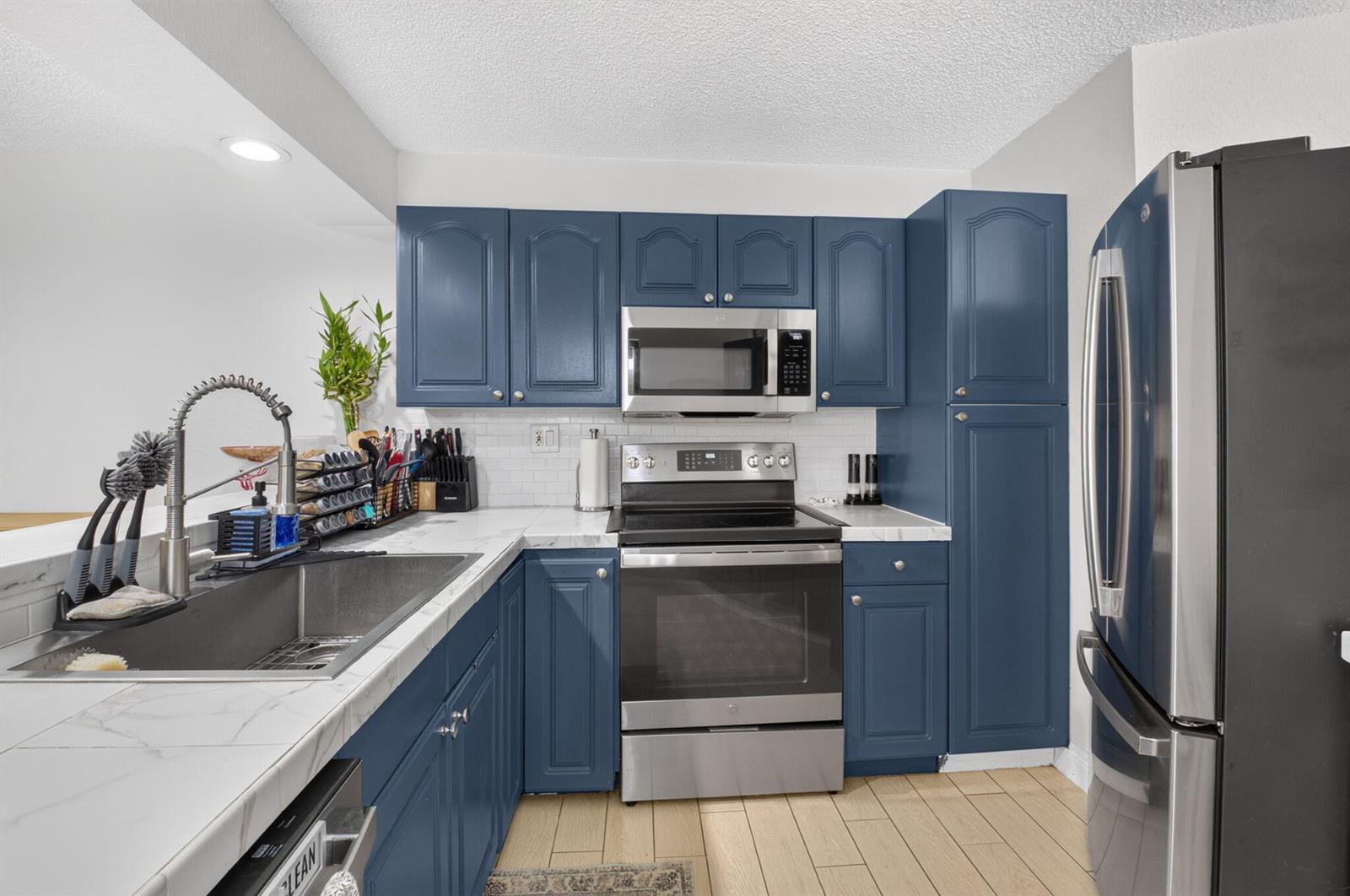 A kitchen features blue cabinets, stainless steel appliances, and white marble-look countertops — 22976 Oxford Place # C, Boca Raton FL 33433, BOCA RATON, FL