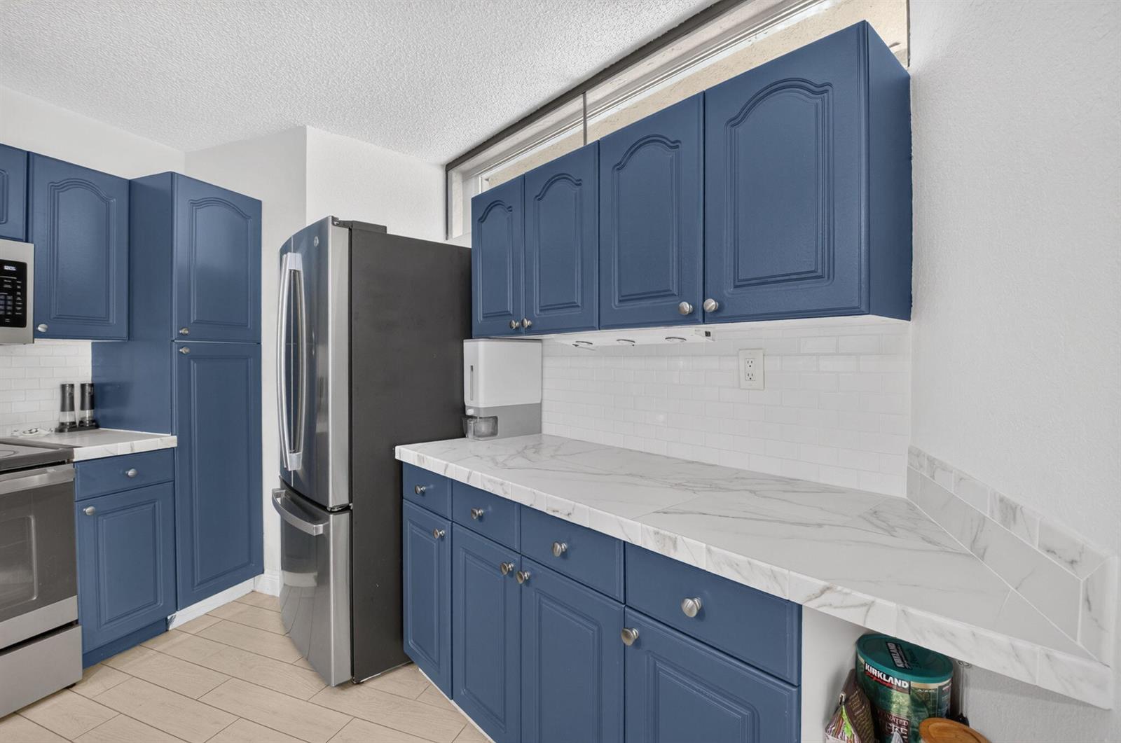 A kitchen features blue cabinets, white subway tile backsplash, and white marble-patterned countertops — 22976 Oxford Place # C, Boca Raton FL 33433, BOCA RATON, FL