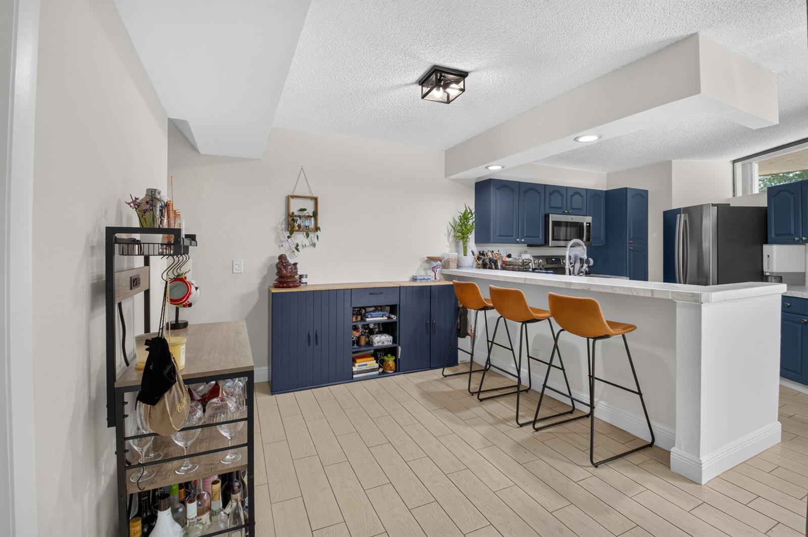 A kitchen features blue cabinets, a breakfast bar with three stools, and light wood flooring — 22976 Oxford Place # C, Boca Raton FL 33433, BOCA RATON, FL