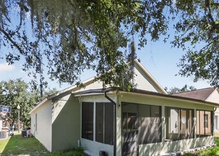 A light-colored house with a screened-in porch sits under large trees on a sunny day — 2016 NEWTOWN ROAD, GROVELAND, FL