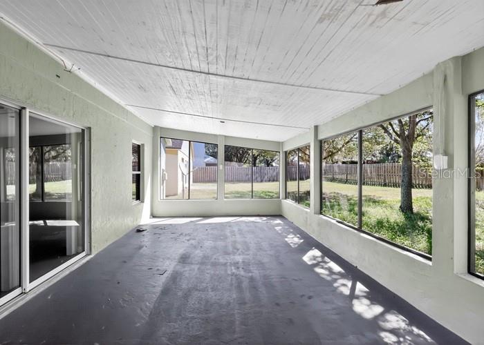 A sunroom with a painted concrete floor, white wood-paneled ceiling, and large windows overlooking a yard — 2016 NEWTOWN ROAD, GROVELAND, FL