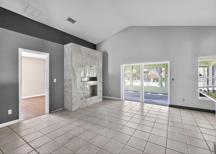 A living room with tiled floors, a marble-tiled fireplace, and sliding glass doors to a patio — 2016 NEWTOWN ROAD, GROVELAND, FL