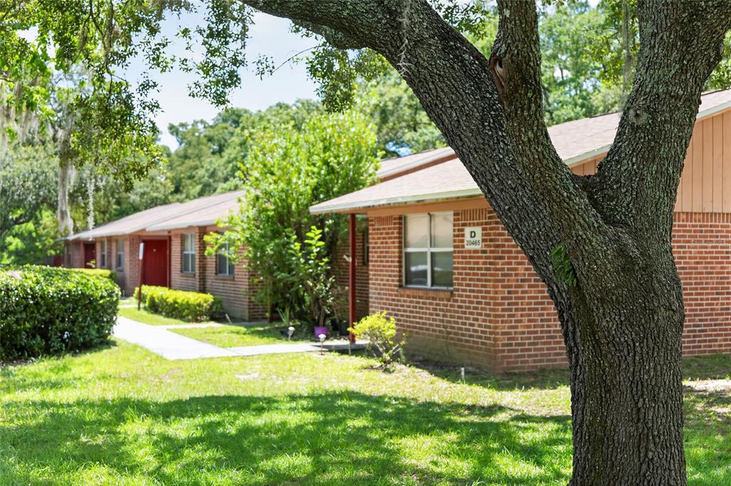 A brick apartment building exterior with a large tree in the foreground — 20420 NW 243RD DRIVE, HIGH SPRINGS, FL
