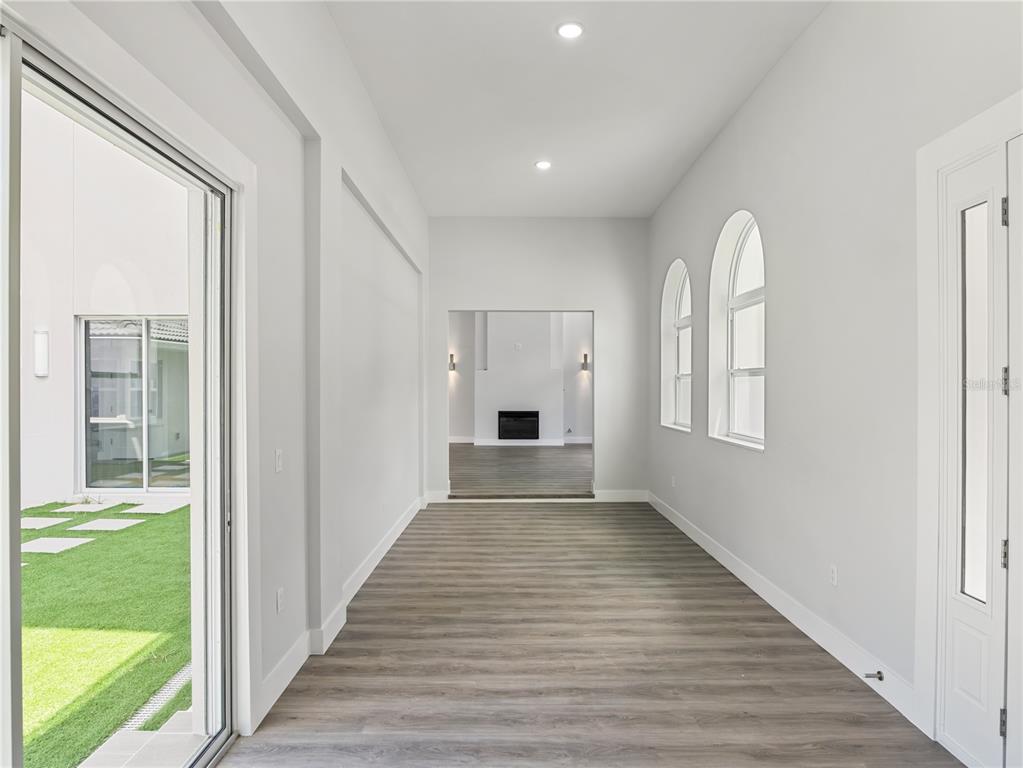 A bright hallway features light wood-look flooring, arched windows, and a view into a living room — 1190 W LAKESHORE DRIVE, CLERMONT, FL