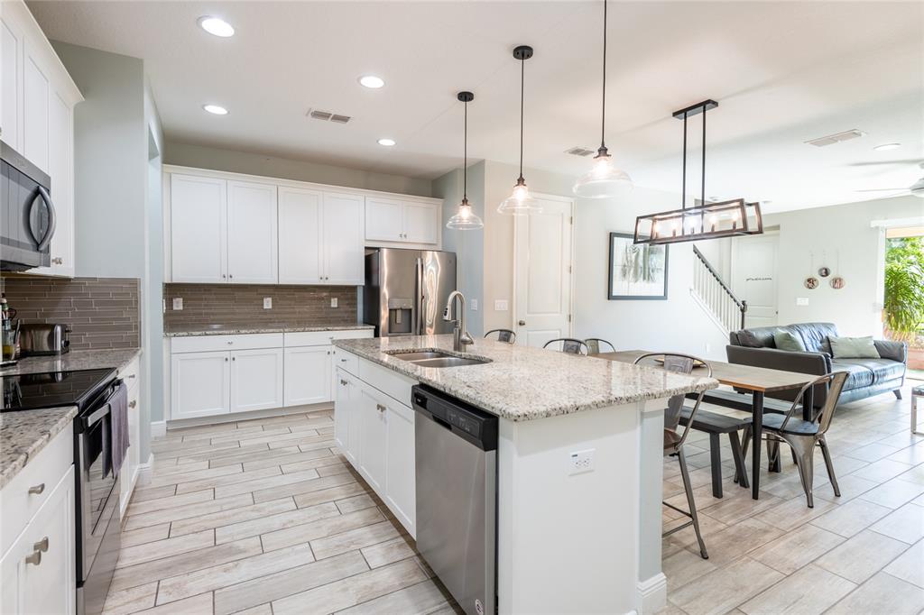A kitchen with white cabinets, granite countertops, and stainless steel appliances opens to a dining area — 17847 ALTHEA BLUE PLACE, LUTZ, FL