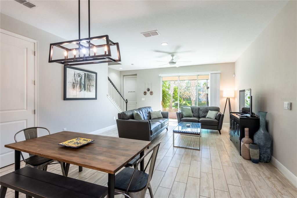 An open-concept living and dining area features tile flooring, a wooden table, and leather sofas — 17847 ALTHEA BLUE PLACE, LUTZ, FL