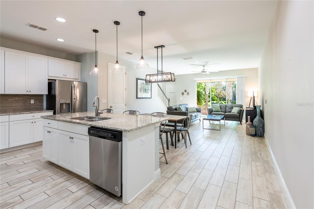 A kitchen with white cabinets and a granite island opens into a living area — 17847 ALTHEA BLUE PLACE, LUTZ, FL