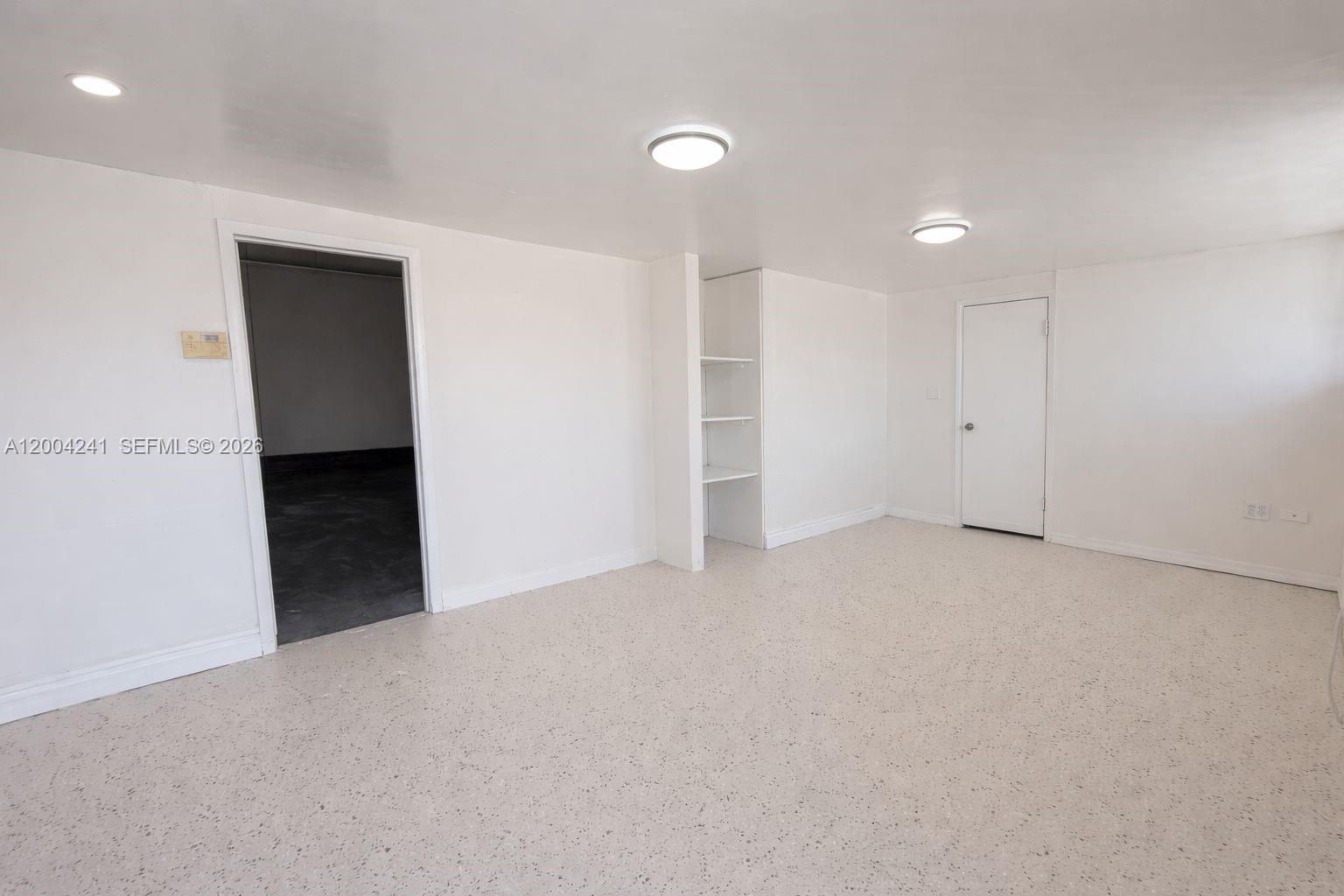 A room with white walls, recessed lighting, speckled flooring, built-in shelving, and two doorways — 7335 NW 32nd Ave # 7345, Miami FL 33147, MIAMI, FL