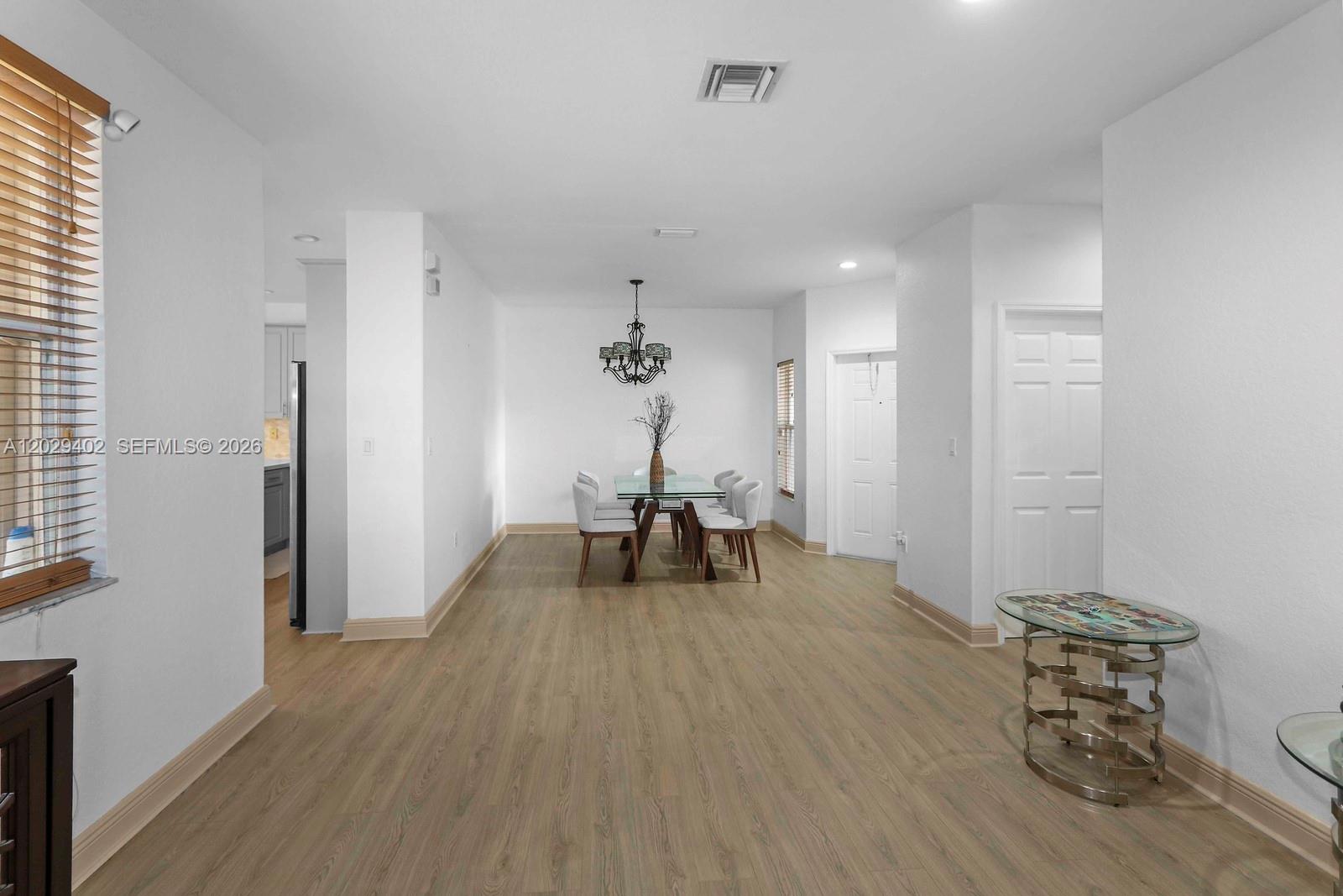 A dining area with a glass table, chandelier, and light wood-look flooring — HOMESTEAD, FL