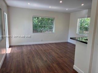 An empty living room with dark wood-look flooring, recessed lighting, and two windows with blinds — 3132 Elizabeth St # B, Miami FL 33133, MIAMI, FL