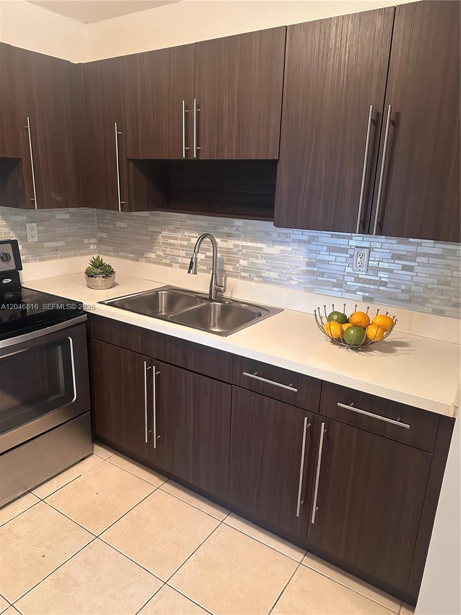 A kitchen features dark wood cabinets, a stainless steel sink, and a tiled backsplash — 1720 Funston St # 203, Hollywood FL 33020, HOLLYWOOD, FL