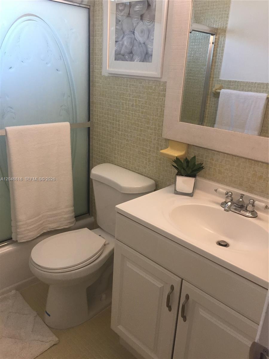 This bathroom features a white vanity, a toilet, a shower stall, and light-colored tile walls — 1720 Funston St # 203, Hollywood FL 33020, HOLLYWOOD, FL