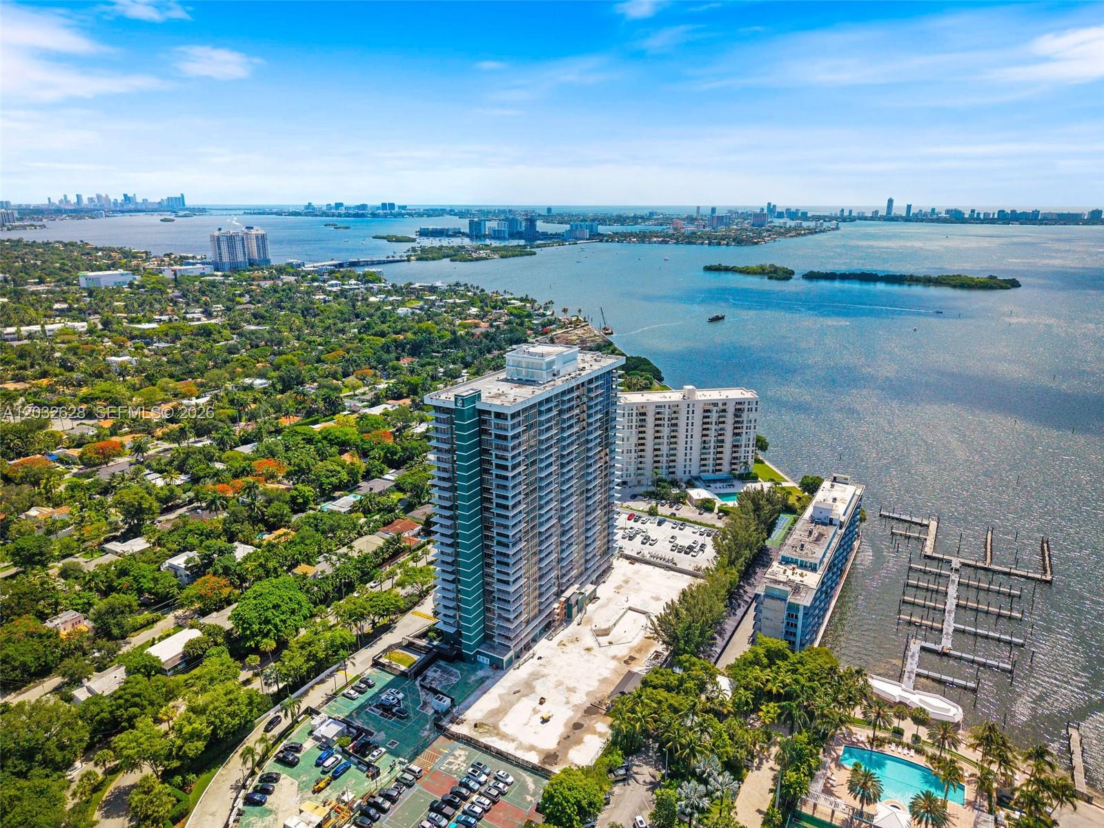 An aerial view shows a tall residential tower surrounded by lush greenery and waterfront docks — 780 NE 69th St # 2404, Miami FL 33138, MIAMI, FL