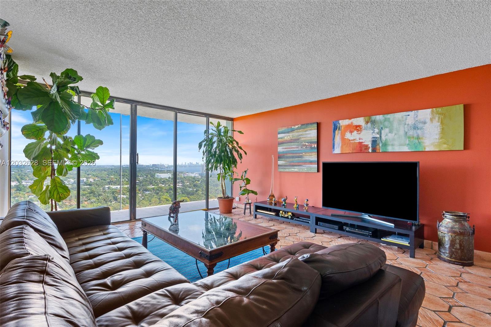 A living room features a leather sofa, orange walls, tile floors, and floor-to-ceiling windows — 780 NE 69th St # 2404, Miami FL 33138, MIAMI, FL