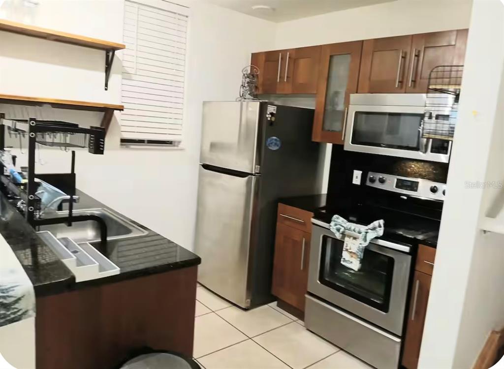 A kitchen features stainless steel appliances, dark wood cabinets, and black granite countertops — 4019 VENETIAN BAY DRIVE UNIT 102, KISSIMMEE, FL
