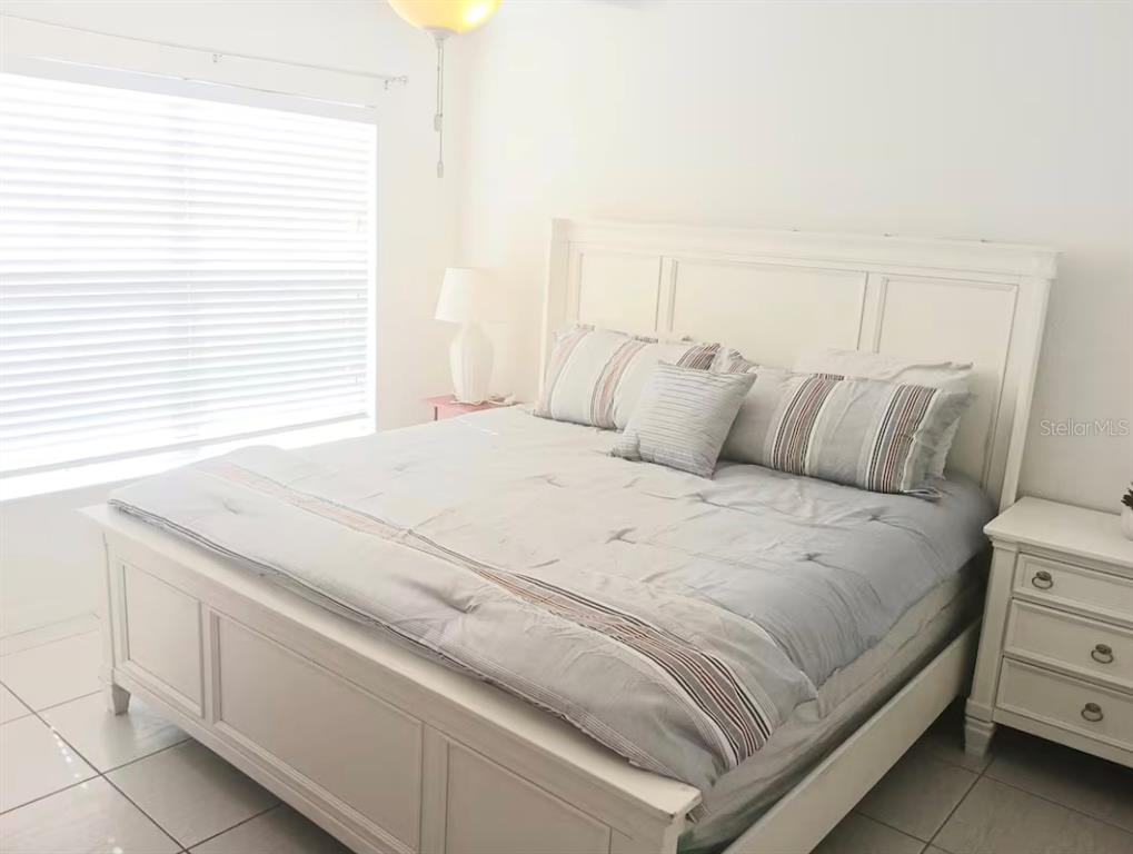 A bedroom features a white bed frame, a light-colored comforter, and a white nightstand — 4019 VENETIAN BAY DRIVE UNIT 102, KISSIMMEE, FL