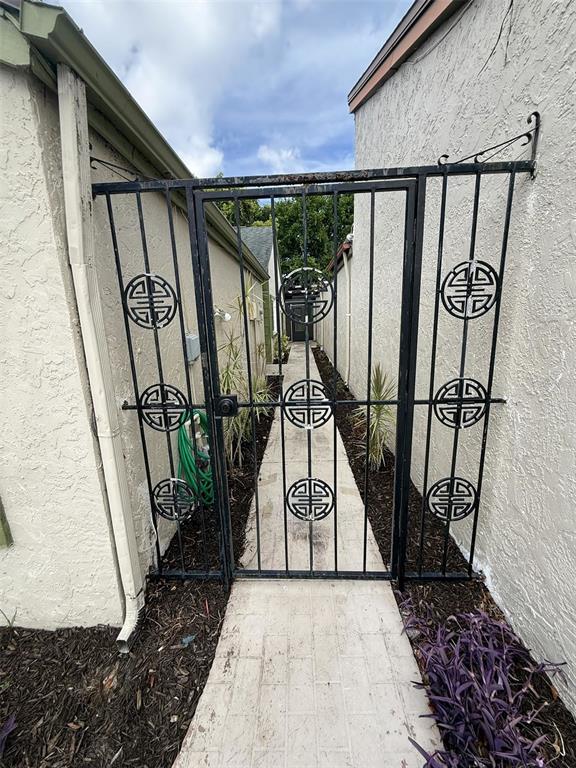 A black metal gate stands between two stucco walls at the entrance of a walkway — 12905 SETTLERS DRIVE, HUDSON, FL