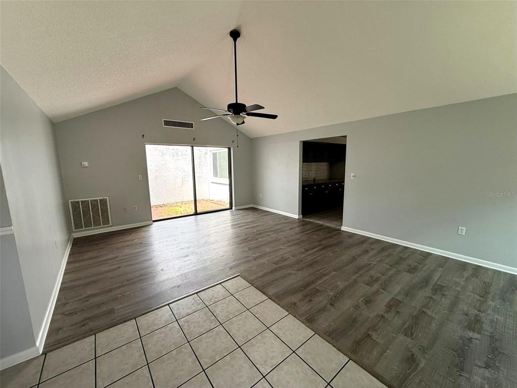 A living room with vaulted ceilings, wood-look flooring, a ceiling fan, and sliding glass doors — 12905 SETTLERS DRIVE, HUDSON, FL