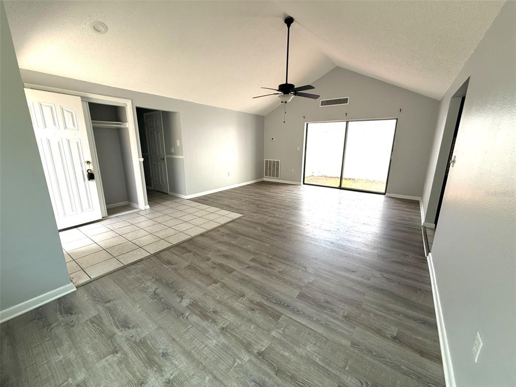 A living room with vaulted ceilings, wood-look flooring, a tiled entryway, and sliding glass doors — 12905 SETTLERS DRIVE, HUDSON, FL