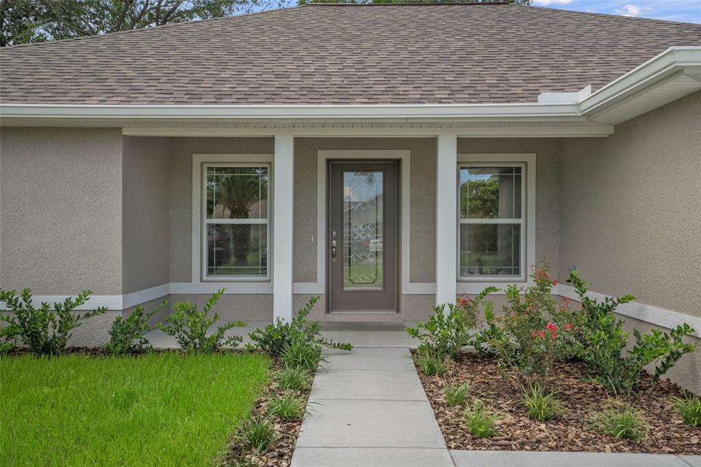 The exterior of a single-story house features a front door, two windows, and landscaping — 16476 KAKAWI ROAD, BROOKSVILLE, FL