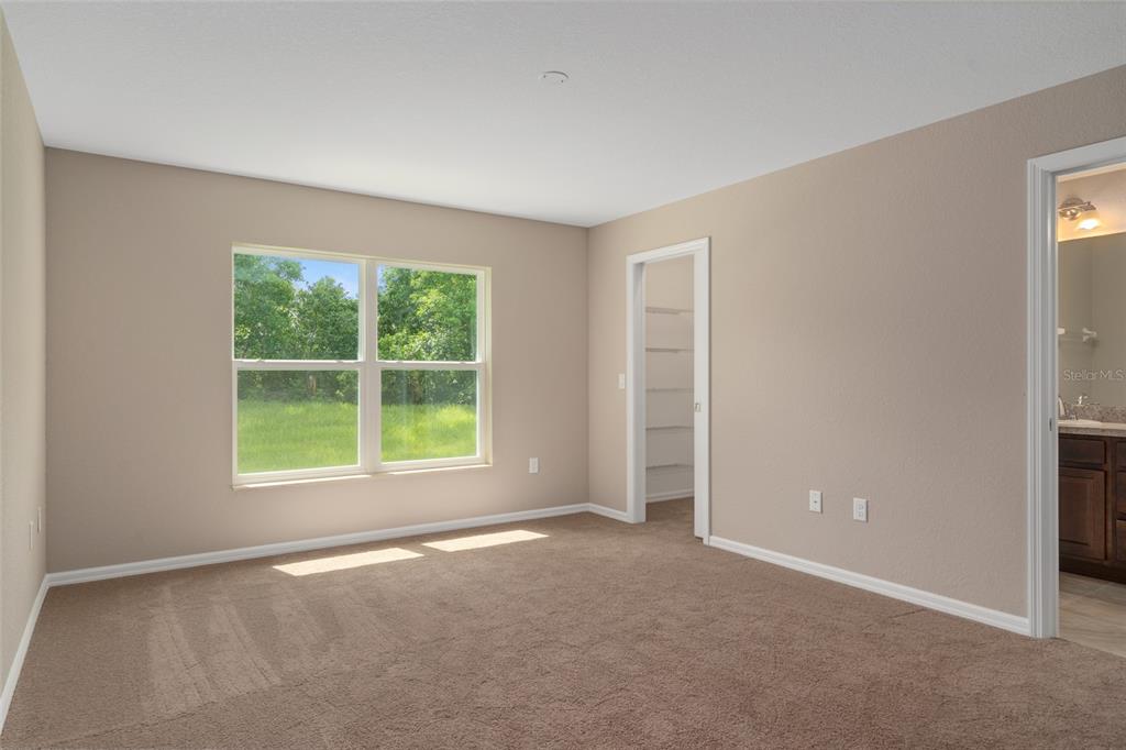 An empty bedroom features beige walls, brown carpet, a window, a closet, and an attached bathroom — 16476 KAKAWI ROAD, BROOKSVILLE, FL