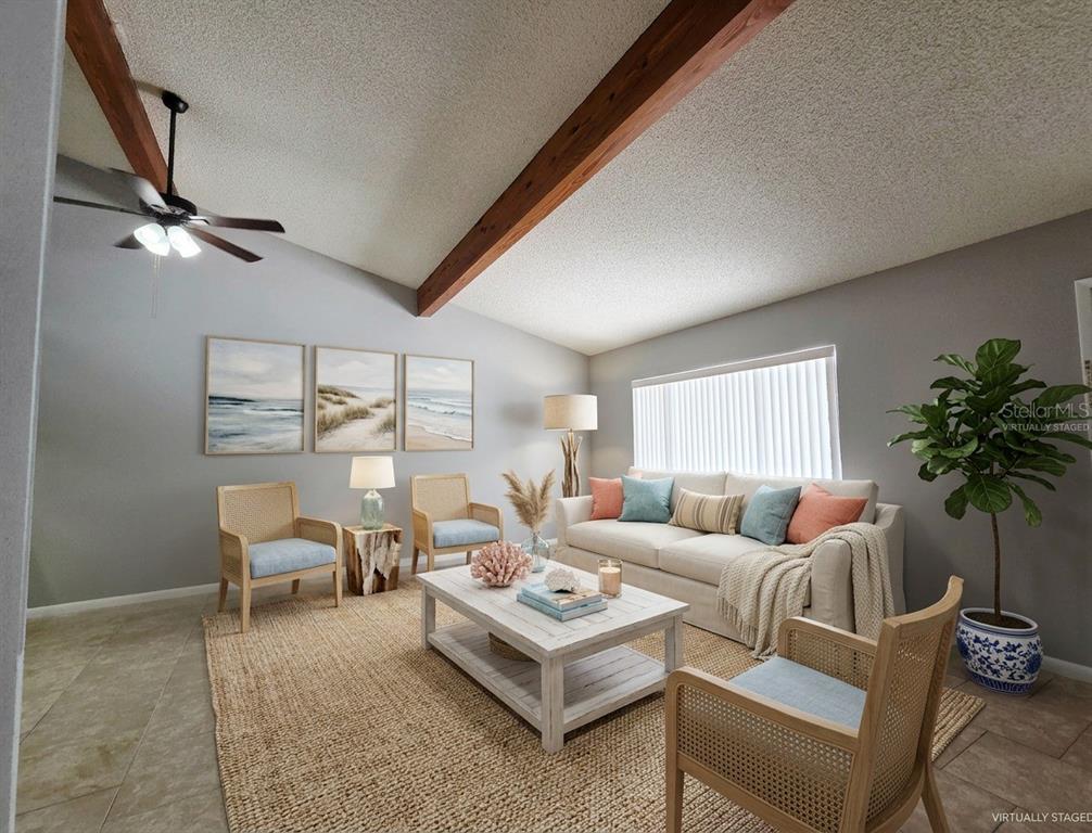 This virtually staged living room features a vaulted ceiling with exposed beams and tile flooring — 104 MAYFAIR PLACE SW, WINTER HAVEN, FL