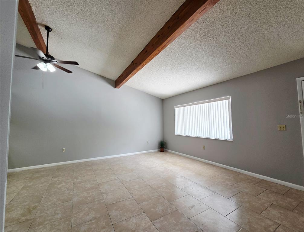 An empty room features light gray walls, tile flooring, and a vaulted ceiling with beams — 104 MAYFAIR PLACE SW, WINTER HAVEN, FL