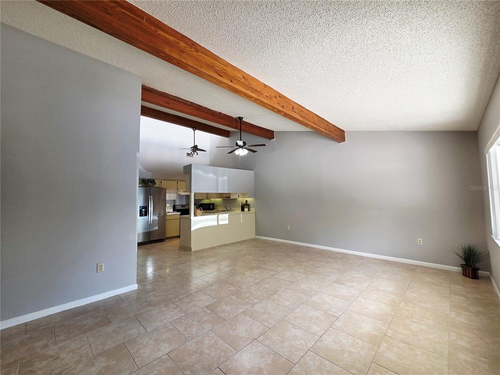 A living room with tile flooring, vaulted ceilings, exposed wooden beams, and an open kitchen — 104 MAYFAIR PLACE SW, WINTER HAVEN, FL