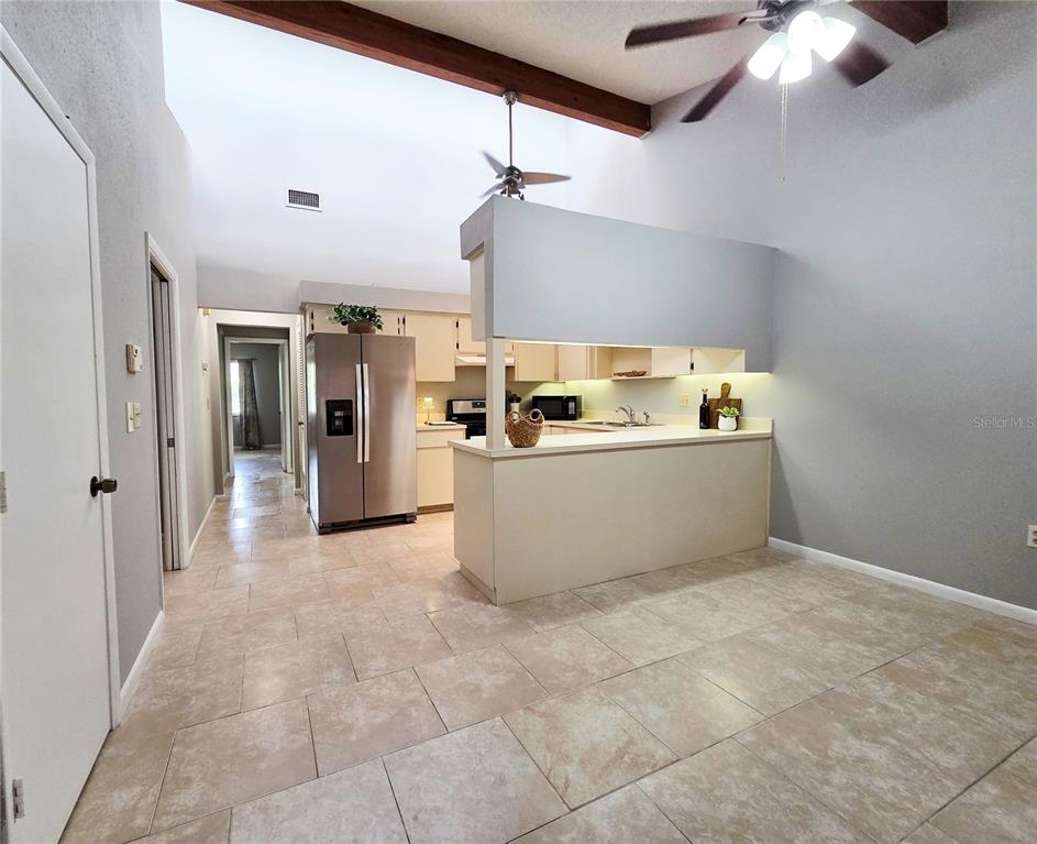 A kitchen with a breakfast bar, stainless steel refrigerator, and tiled floors under vaulted ceilings — 104 MAYFAIR PLACE SW, WINTER HAVEN, FL