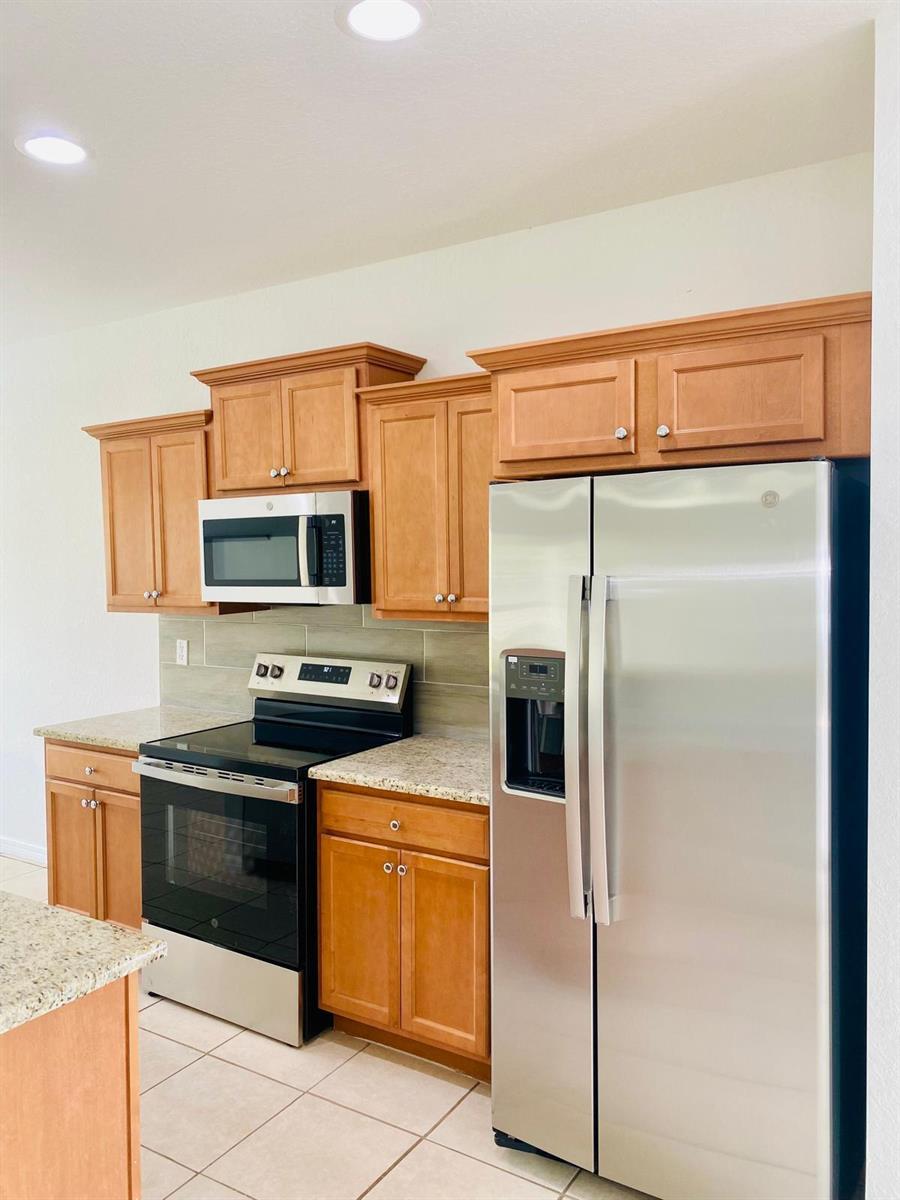 A kitchen features wood cabinets, granite countertops, stainless steel appliances, and a tile backsplash — 9312 Natures Way, Fort Pierce FL 34945, FORT PIERCE, FL