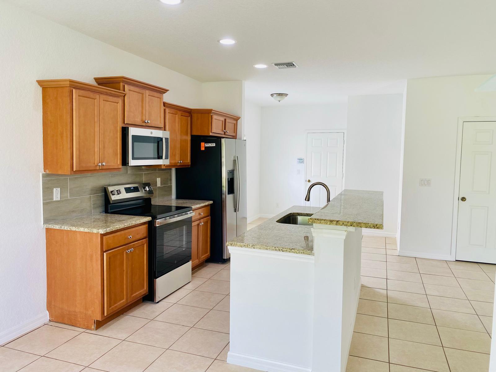A kitchen features wood cabinets, granite countertops, stainless steel appliances, and a central island — 9312 Natures Way, Fort Pierce FL 34945, FORT PIERCE, FL