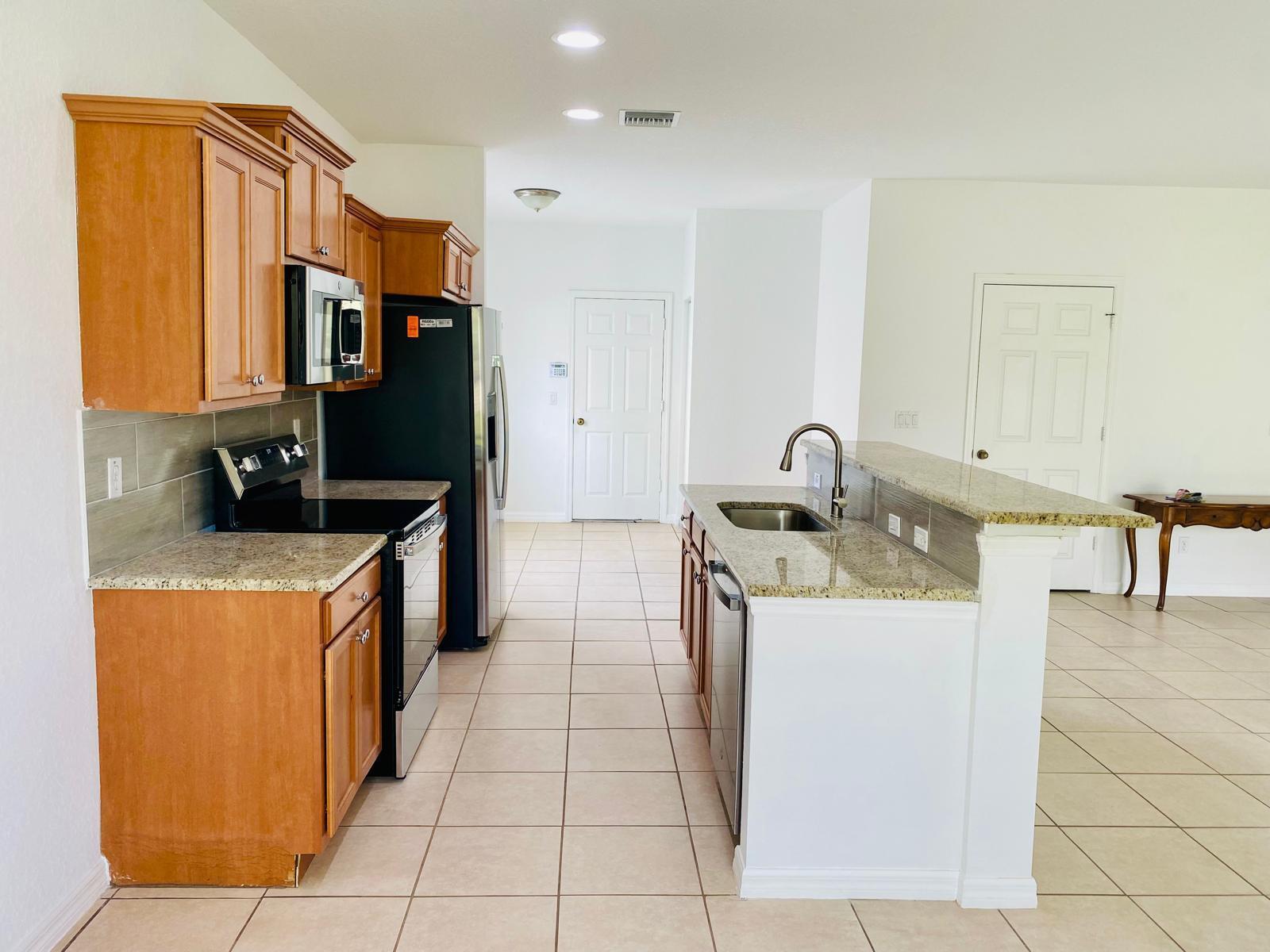 A kitchen features wood cabinets, granite countertops, stainless steel appliances, and tile flooring — 9312 Natures Way, Fort Pierce FL 34945, FORT PIERCE, FL