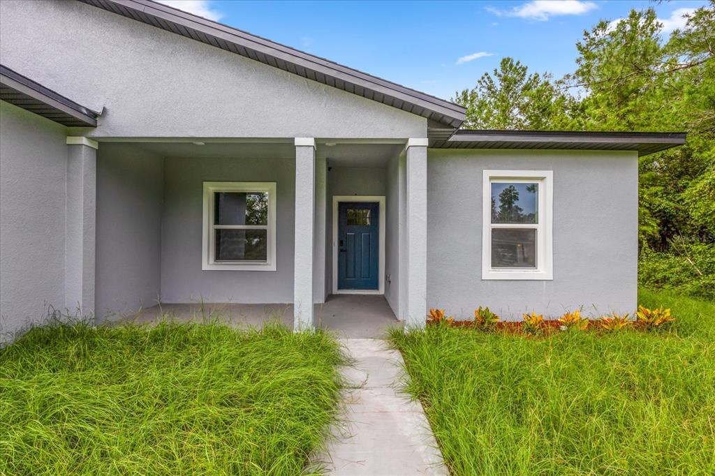 The back exterior of a single-story house features gray stucco walls, a covered patio, and two windows — 16862 SW 40TH CIR, OCALA, FL