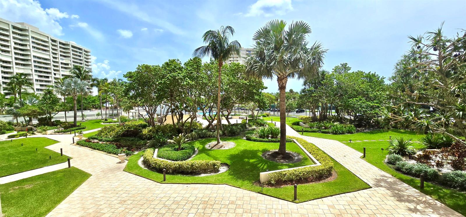 A landscaped courtyard with palm trees, manicured lawns, and paved walkways between apartment buildings — 4101 N Ocean Boulevard # 207, Boca Raton FL 33431, BOCA RATON, FL