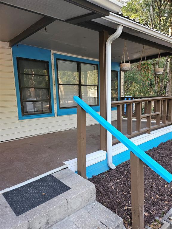 A covered porch features a concrete floor, blue trim, and a wooden railing — 10250 SE 108TH TERRACE ROAD, OCALA, FL