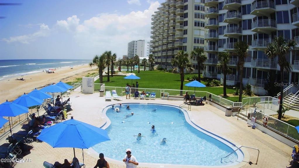 An outdoor swimming pool sits beside a beach resort building with balconies overlooking the ocean — 1155 OCEAN SHORE BOULEVARD UNIT 102, ORMOND BEACH, FL