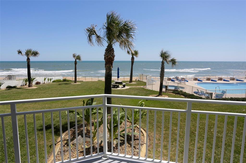 A balcony view overlooking a grassy lawn, palm trees, a swimming pool, and the ocean — 1155 OCEAN SHORE BOULEVARD UNIT 102, ORMOND BEACH, FL