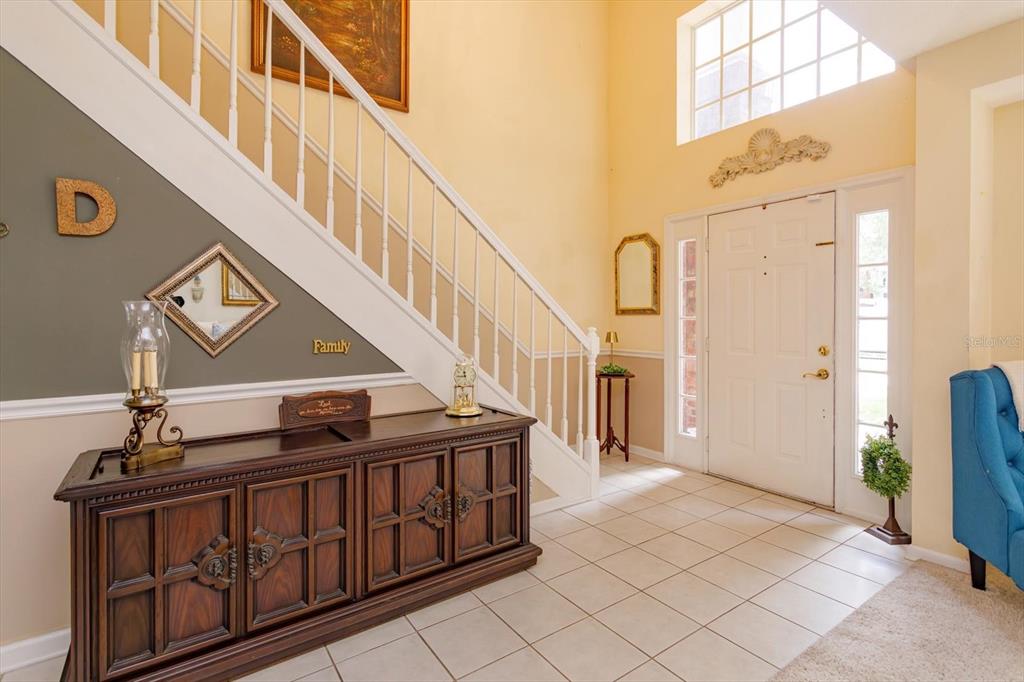 An entryway features a tiled floor, a wooden console table, and a staircase with white railings — 50 OAK BEND COURT, OVIEDO, FL