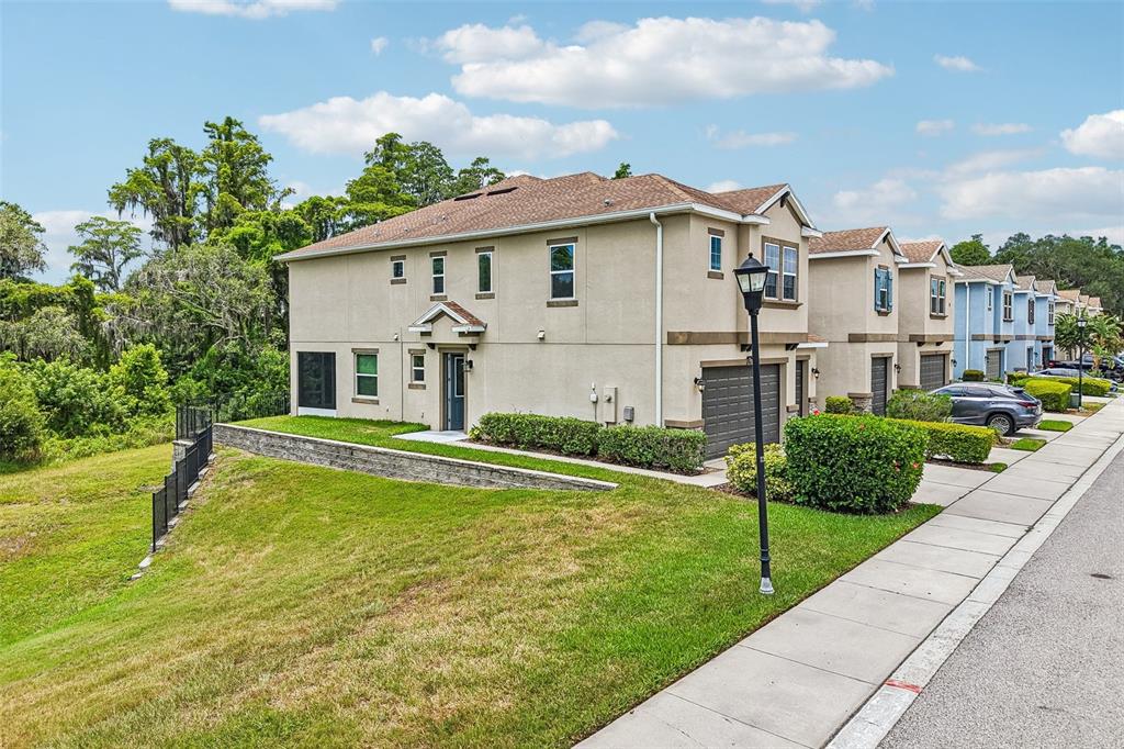 An exterior view of a multi-unit townhouse complex with a grassy slope and sidewalk — 6706 ROCKY PARK STREET, TAMPA, FL