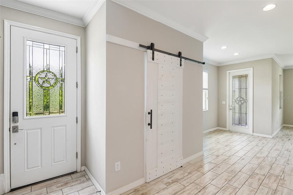 An entryway features a white barn door, light wood-look tile flooring, and two glass-paneled doors — 6706 ROCKY PARK STREET, TAMPA, FL
