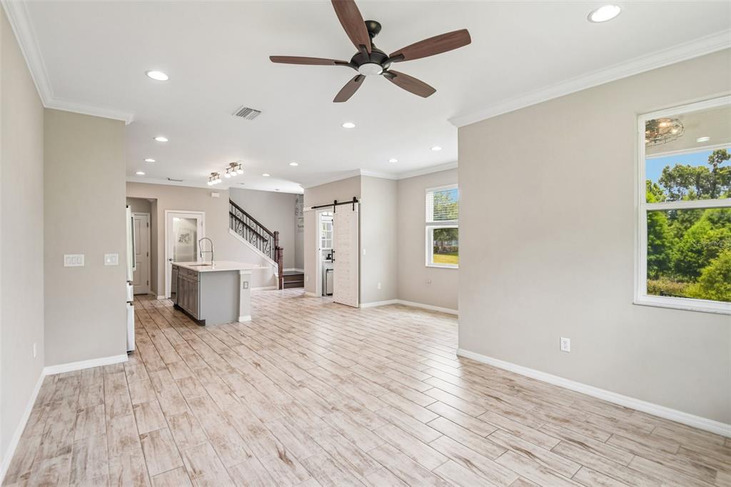 A bright, open-concept living area features wood-look tile flooring, a ceiling fan, and a kitchen — 6706 ROCKY PARK STREET, TAMPA, FL