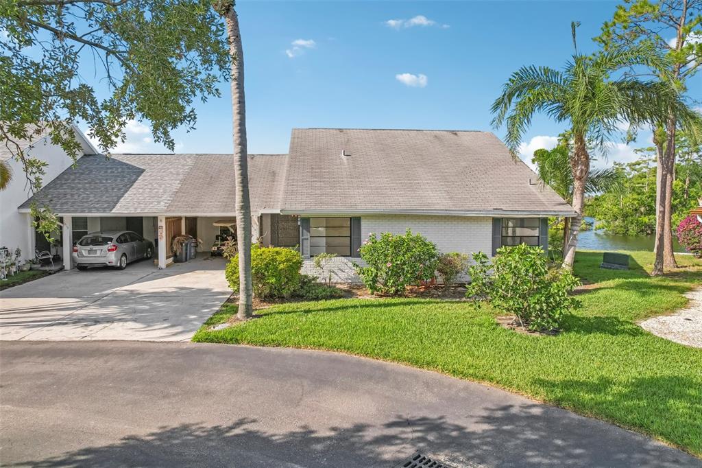 A single-story house with a carport, a paved driveway, and a grassy lawn near water — 1613 COMFY COURT, SUN CITY CENTER, FL