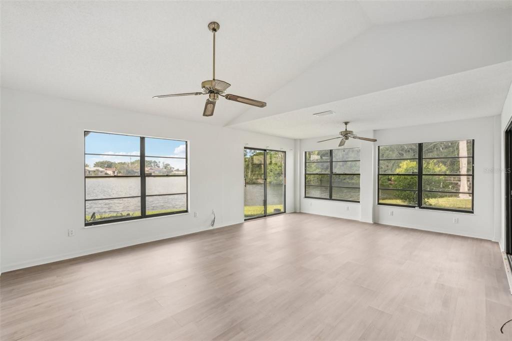 A bright living room features light wood-look flooring, two ceiling fans, and large windows overlooking water — 1613 COMFY COURT, SUN CITY CENTER, FL